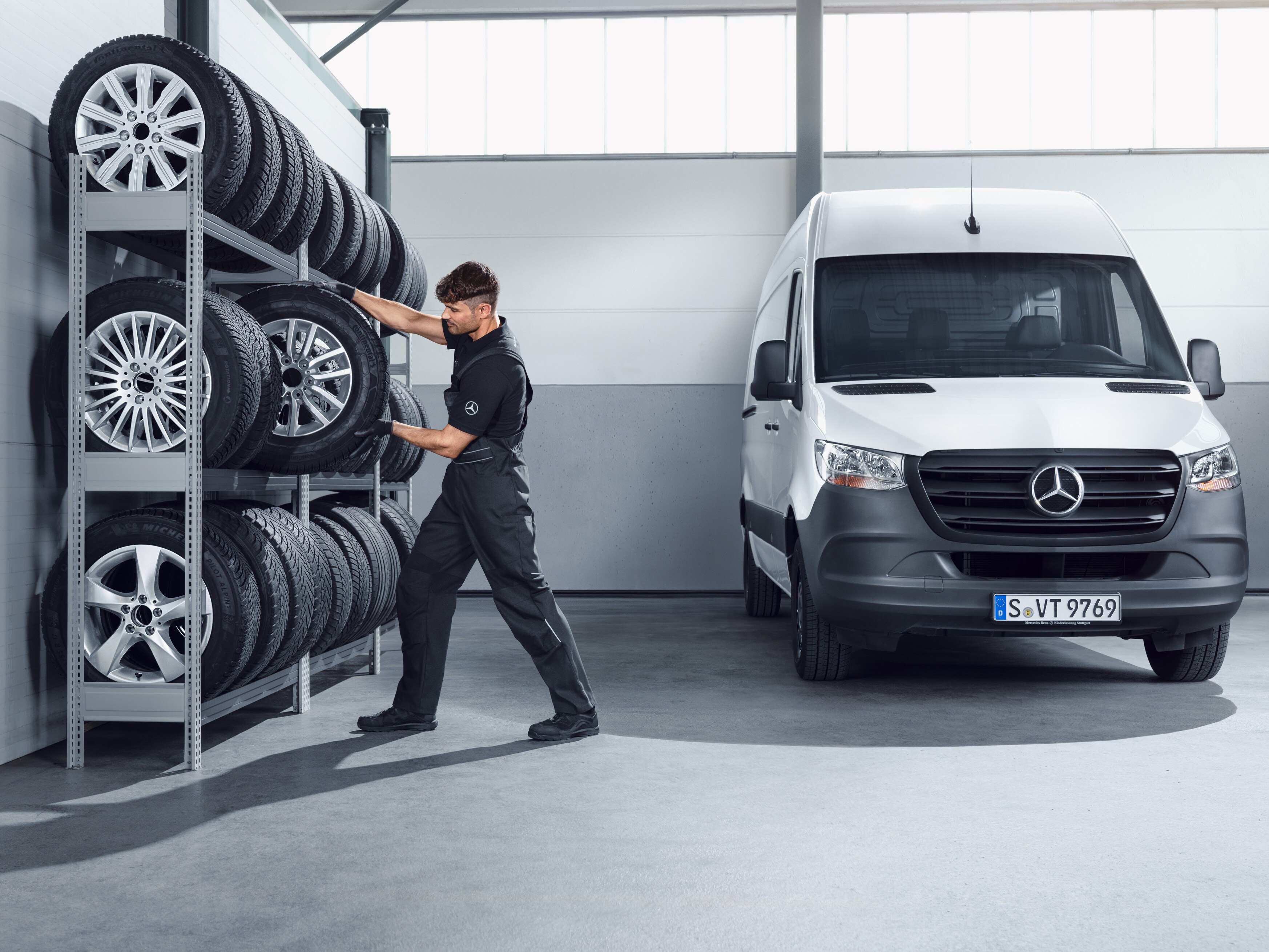 Mekaniker plockar ner Mercedes-Benz kompletta vinterhjul till en vit Sprinter från verkstadshyllan.