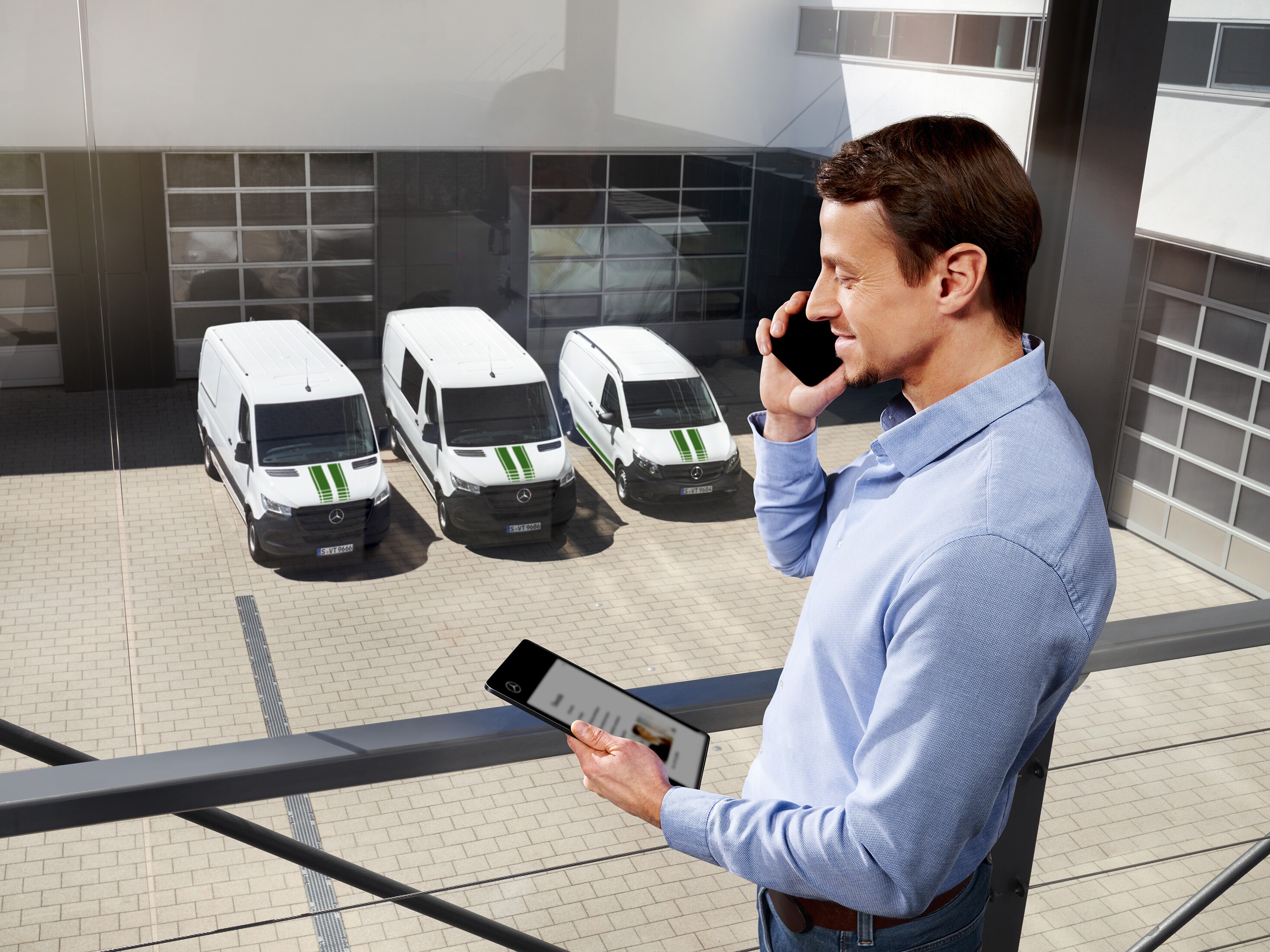 Man med surfplatta och mobiltelefon framför tre Mercedes-Benz transportbilar.