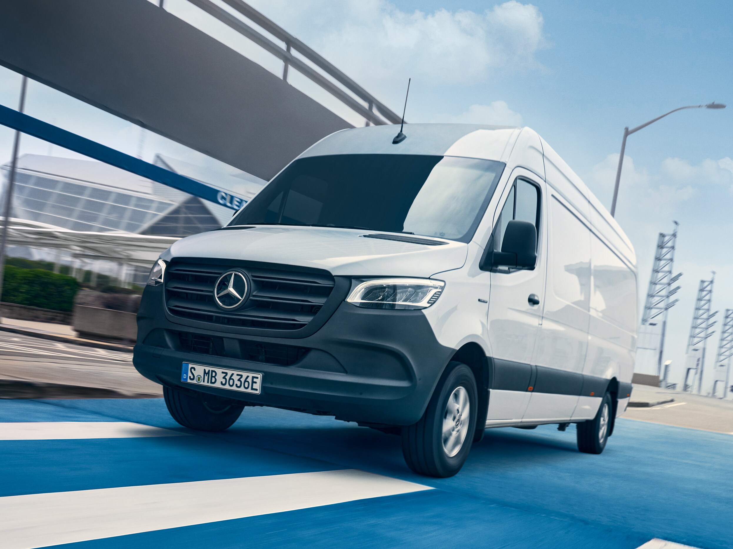 En vit Mercedes-Benz Sprinter kör på en väg genom en stad.