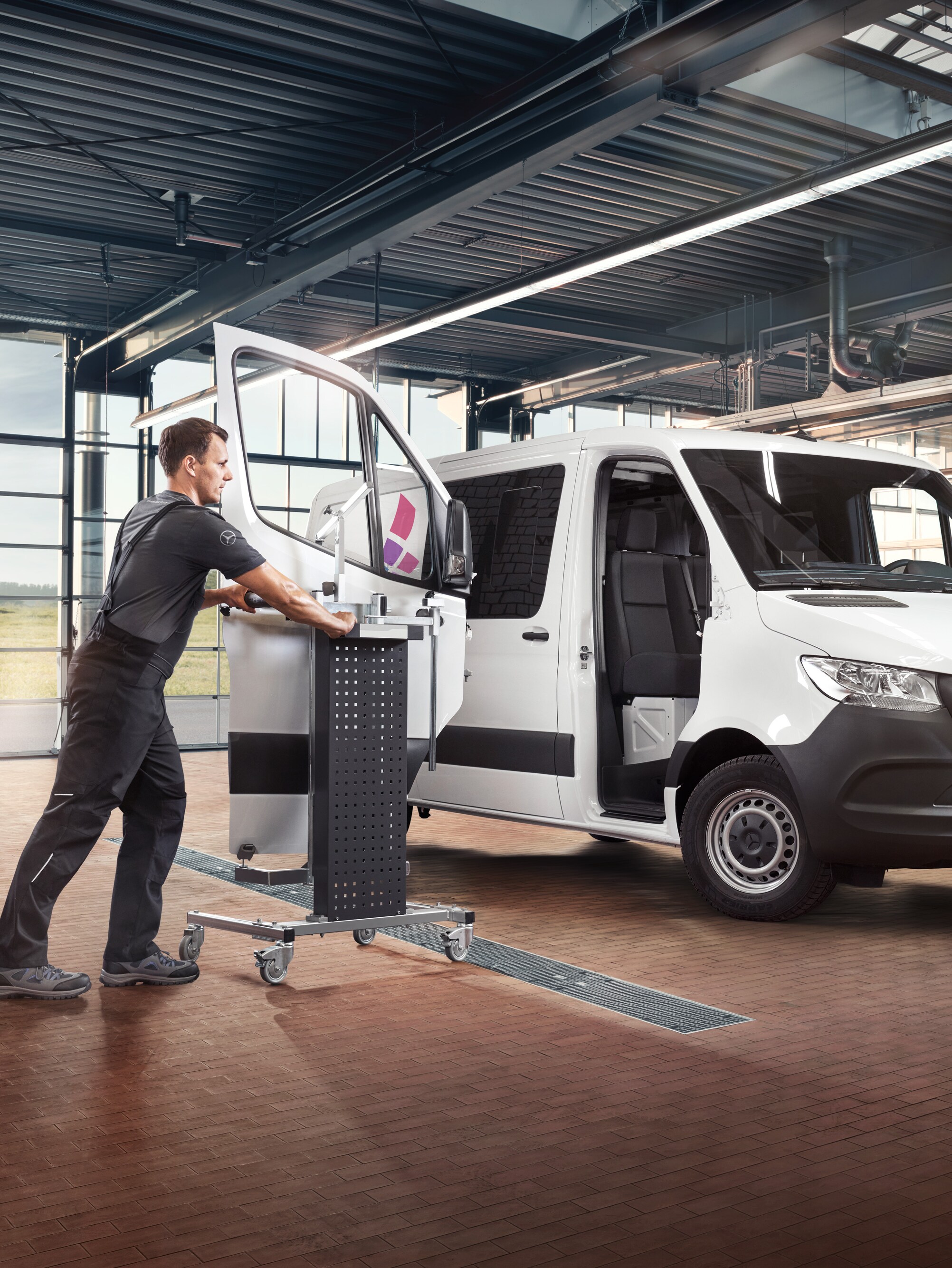 En tekniker servar passagerardörren på en vit Mercedes-Benz Sprinter-transportbil.