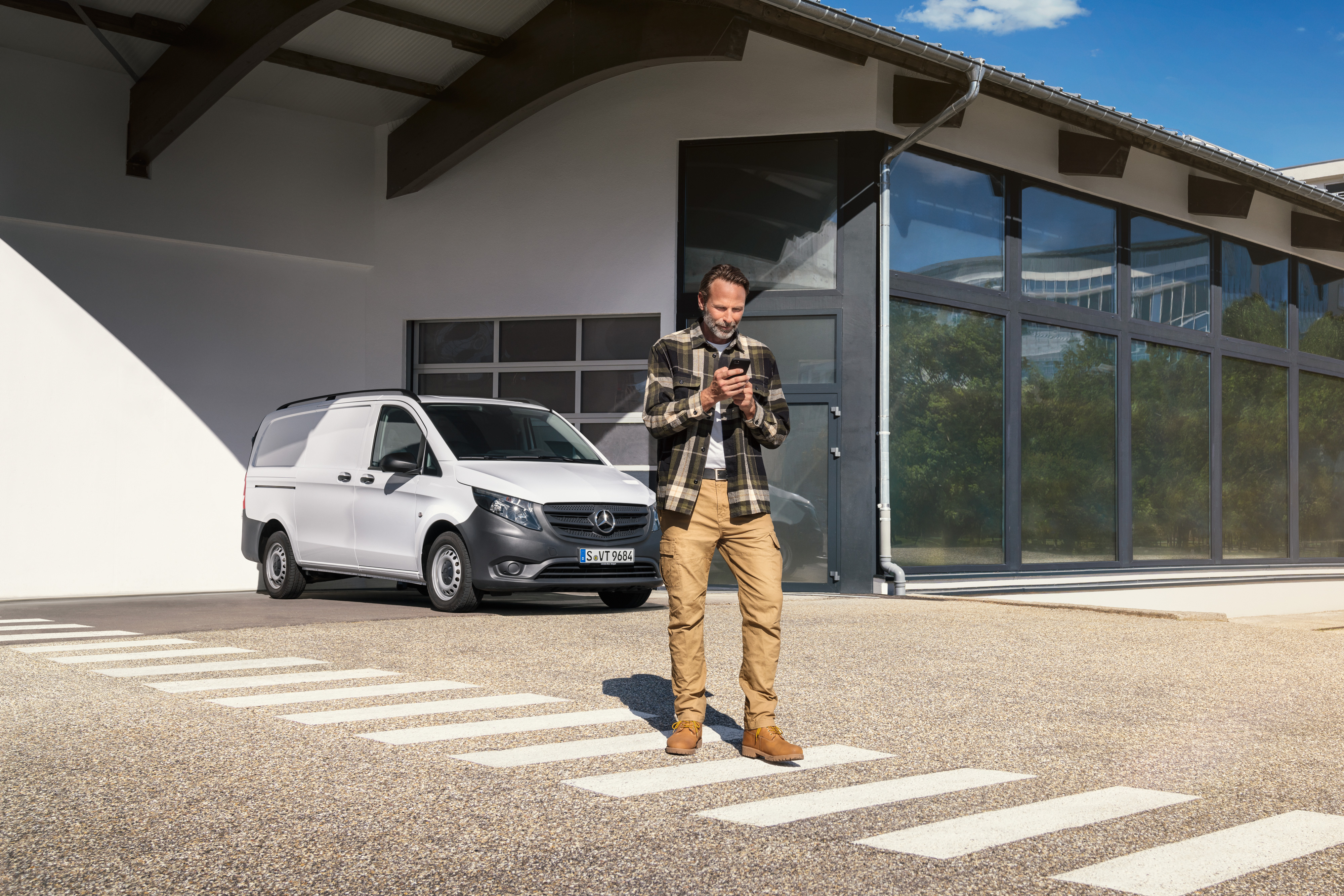 Mercedes-Benz | Service av elbilar | Digitalt stöd En man står framför en vit Mercedes-Benz Vito-transportbil och använder sin smartphone.