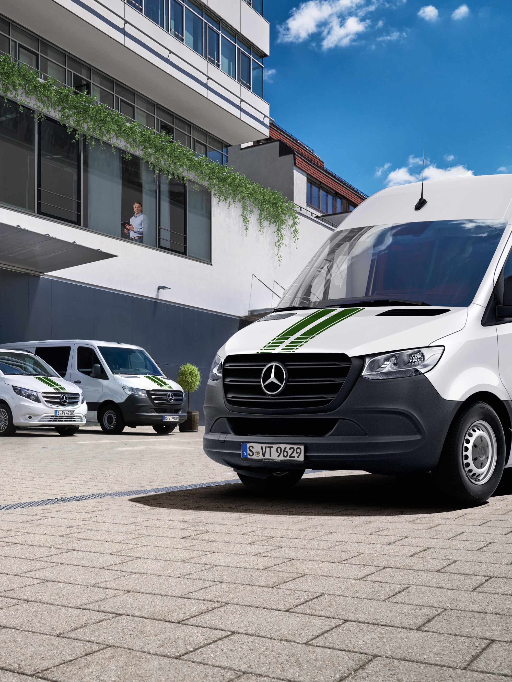 En vagnpark bestående av vita Mercedes-Benz-transportbilar framför en kontorsbyggnad en solig dag med blå himmel.