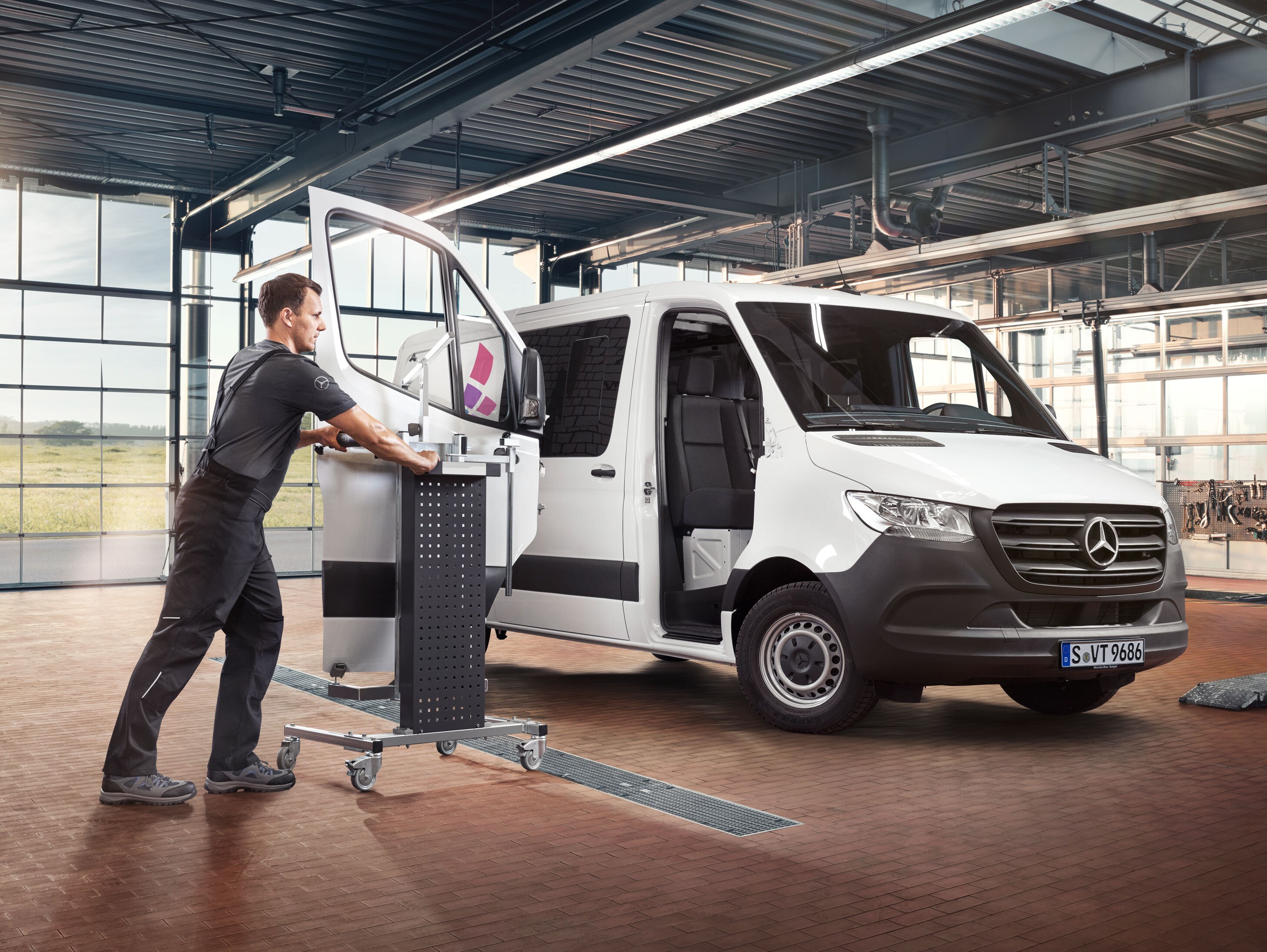 En mekaniker monterar dörren på en vit Mercedes-Benz Sprinter.