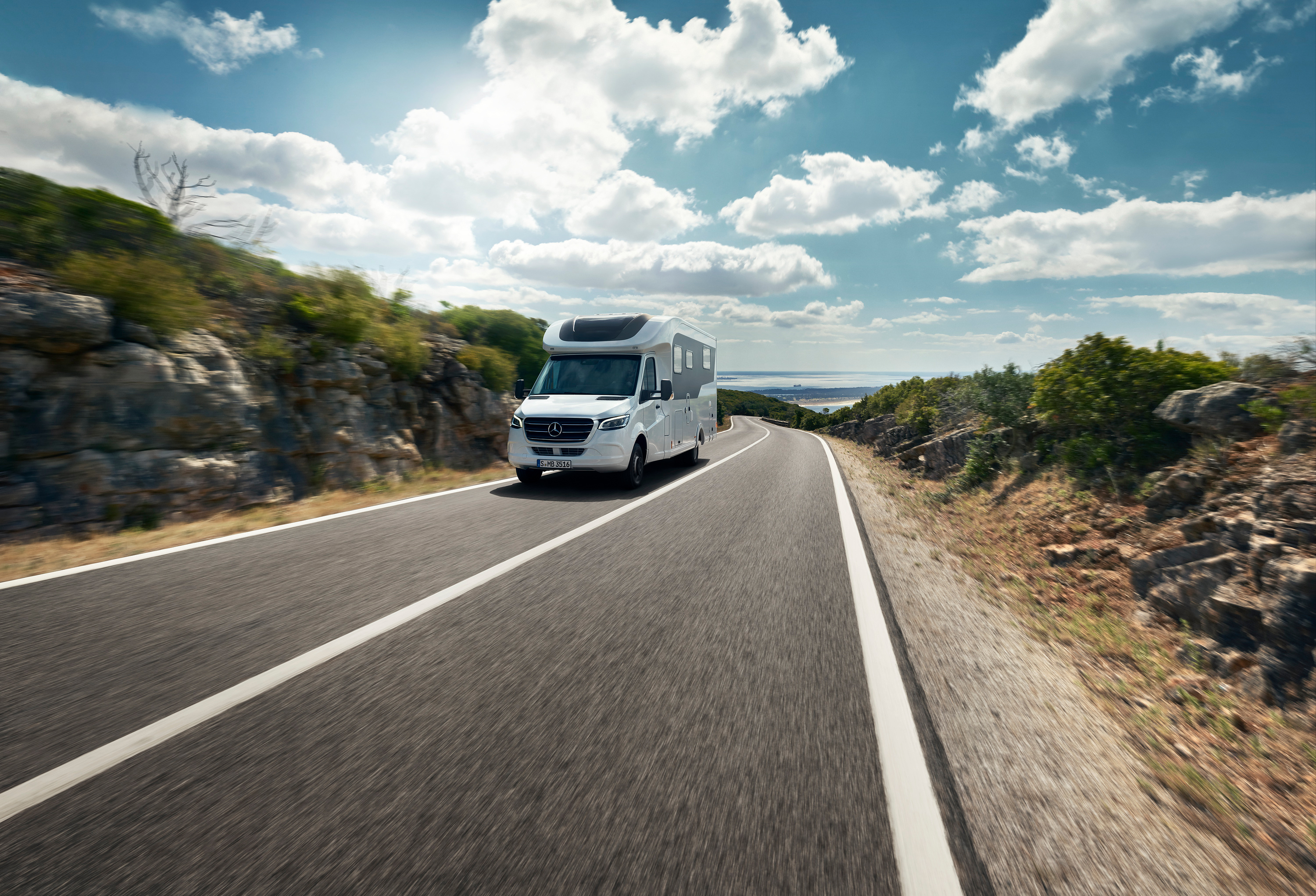 Sprinter Husbil | Campingbilar & husbilar | Mercedes-Benz Transportbilar Mercedes-Benz Sprinter husbil kör uppför bergsväg med vatten i horisonten