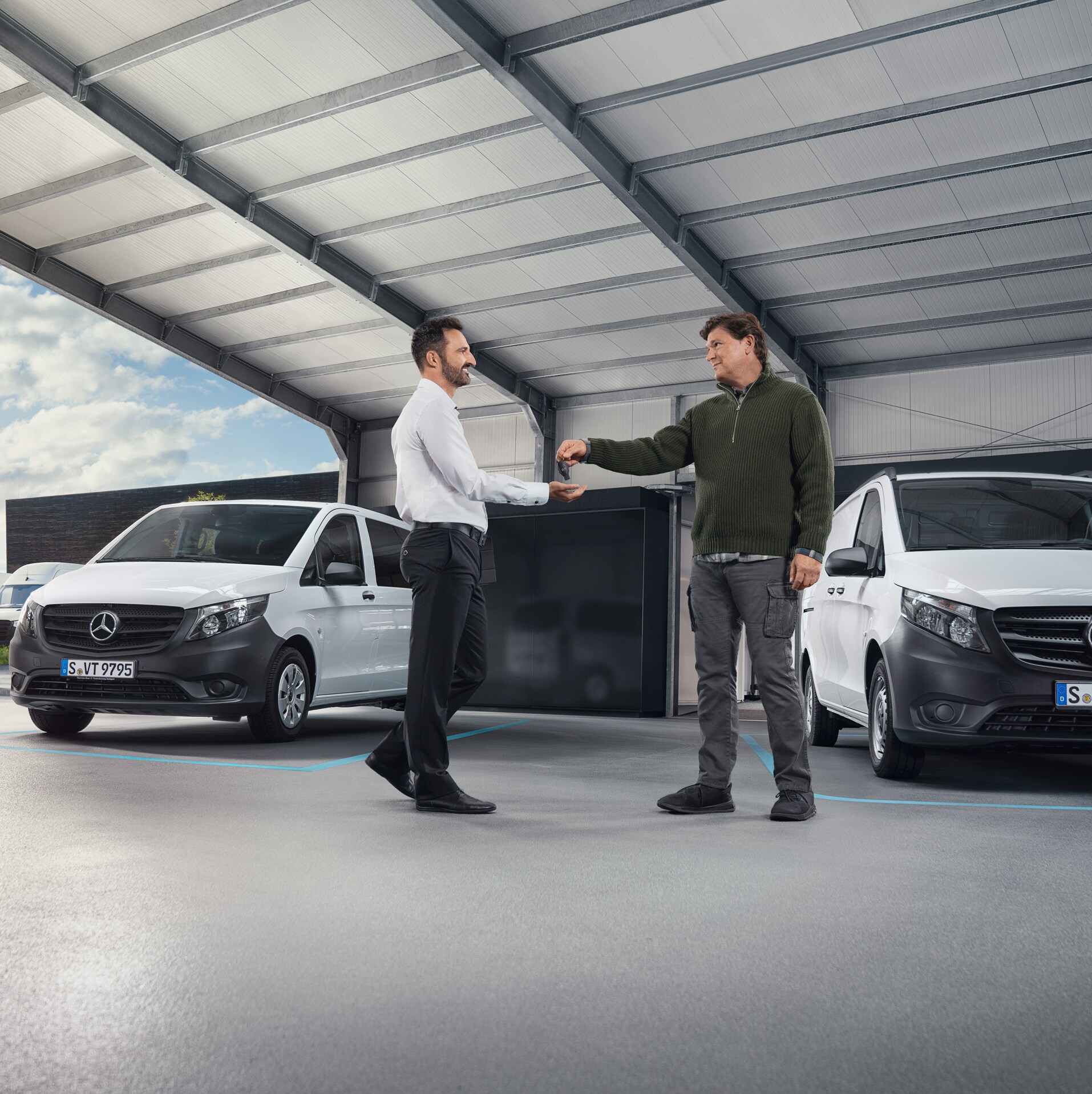 Två män diskuterar framför en rad vita Mercedes-Benz skåpbilar i en hall