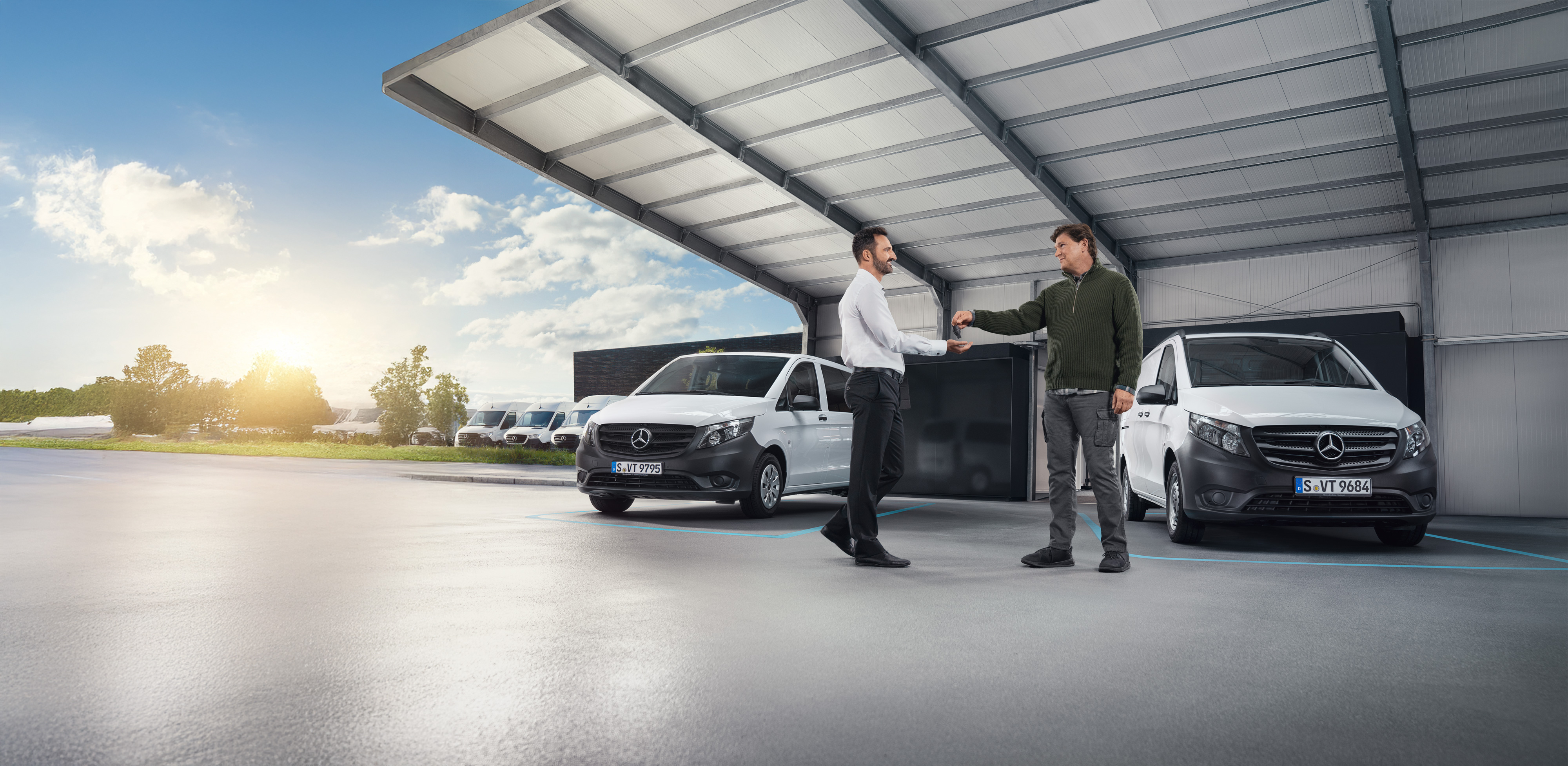 Mercedes-Benz | Van Care | Individuell hjälp Två män diskuterar framför en rad vita Mercedes-Benz skåpbilar i en hall