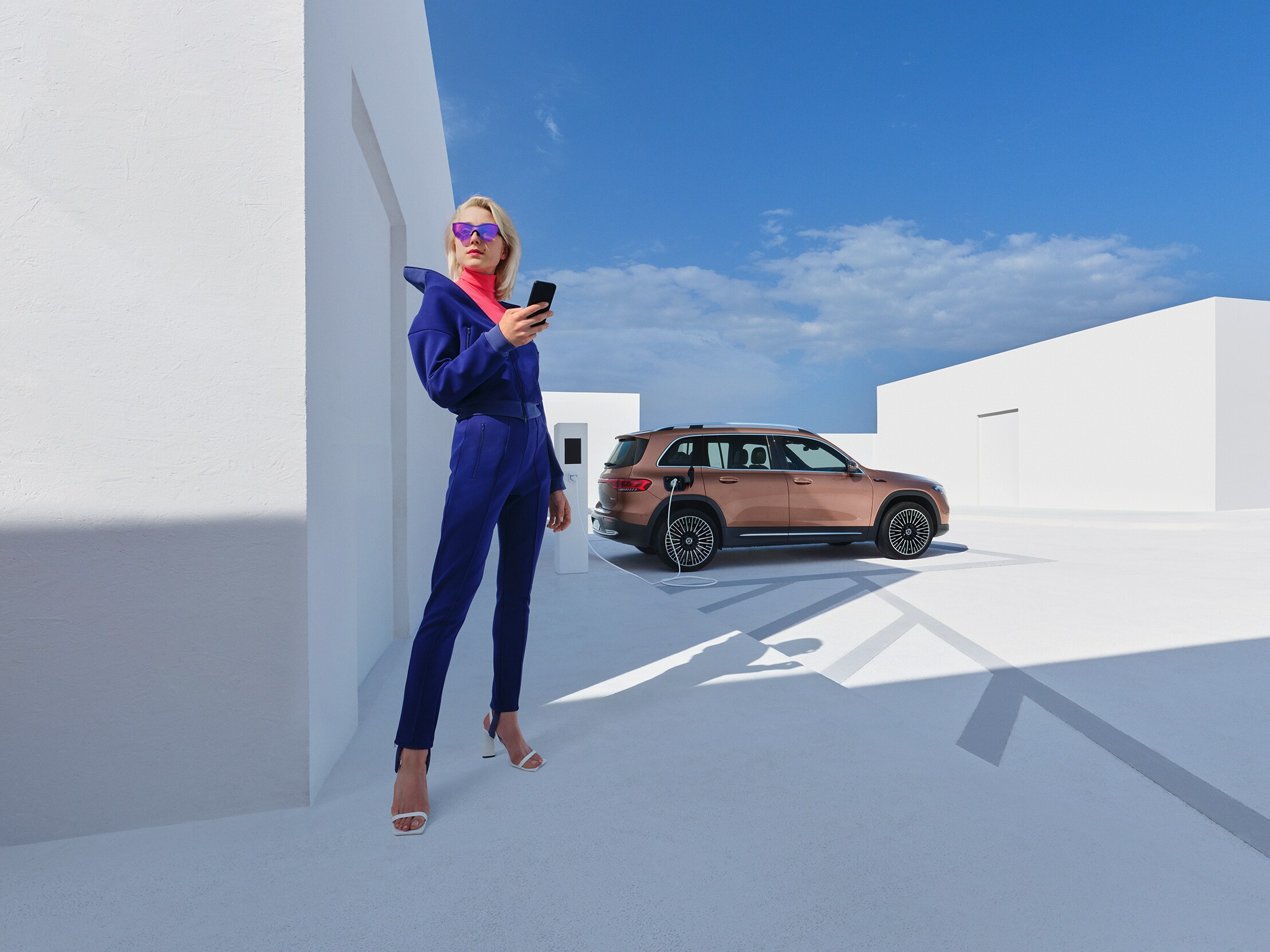 Kvinna står med smartphone medan hennes Mercedes-Benz SUV laddas i bakgrunden