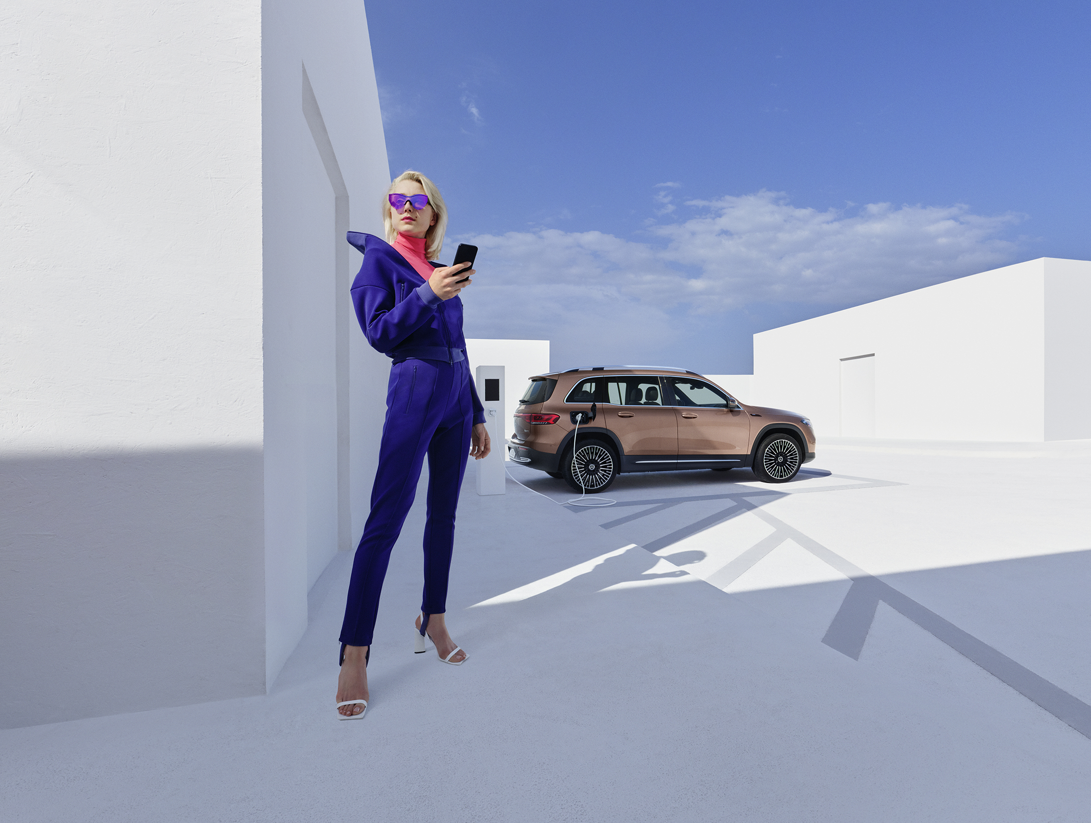 Laddhybrid SUV | Mercedes-Benz Kvinna står med smartphone medan hennes Mercedes-Benz SUV laddas i bakgrunden