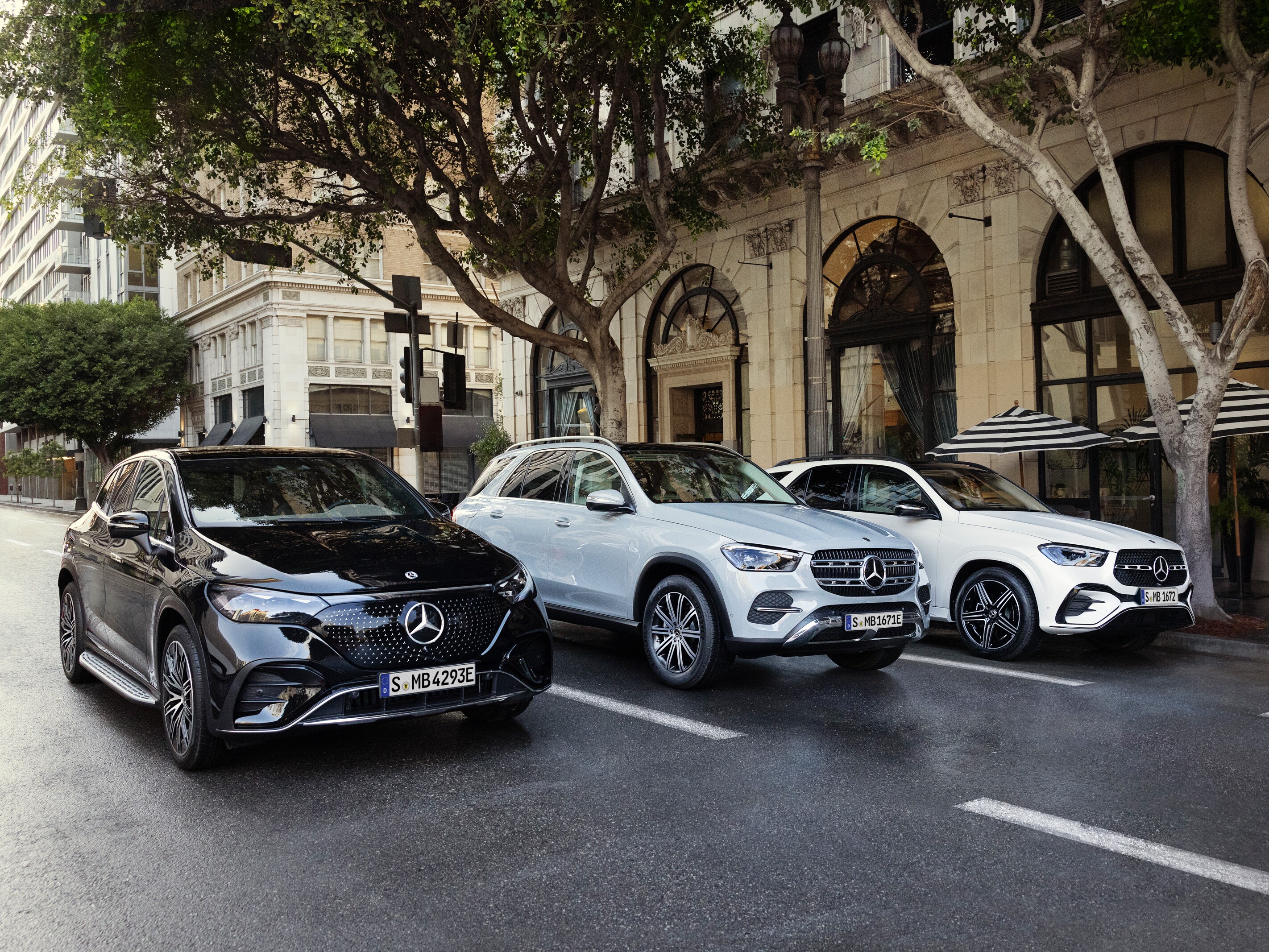 Tre olika Mercedes-Benz modeller sida vid sida på en väg i storstad.