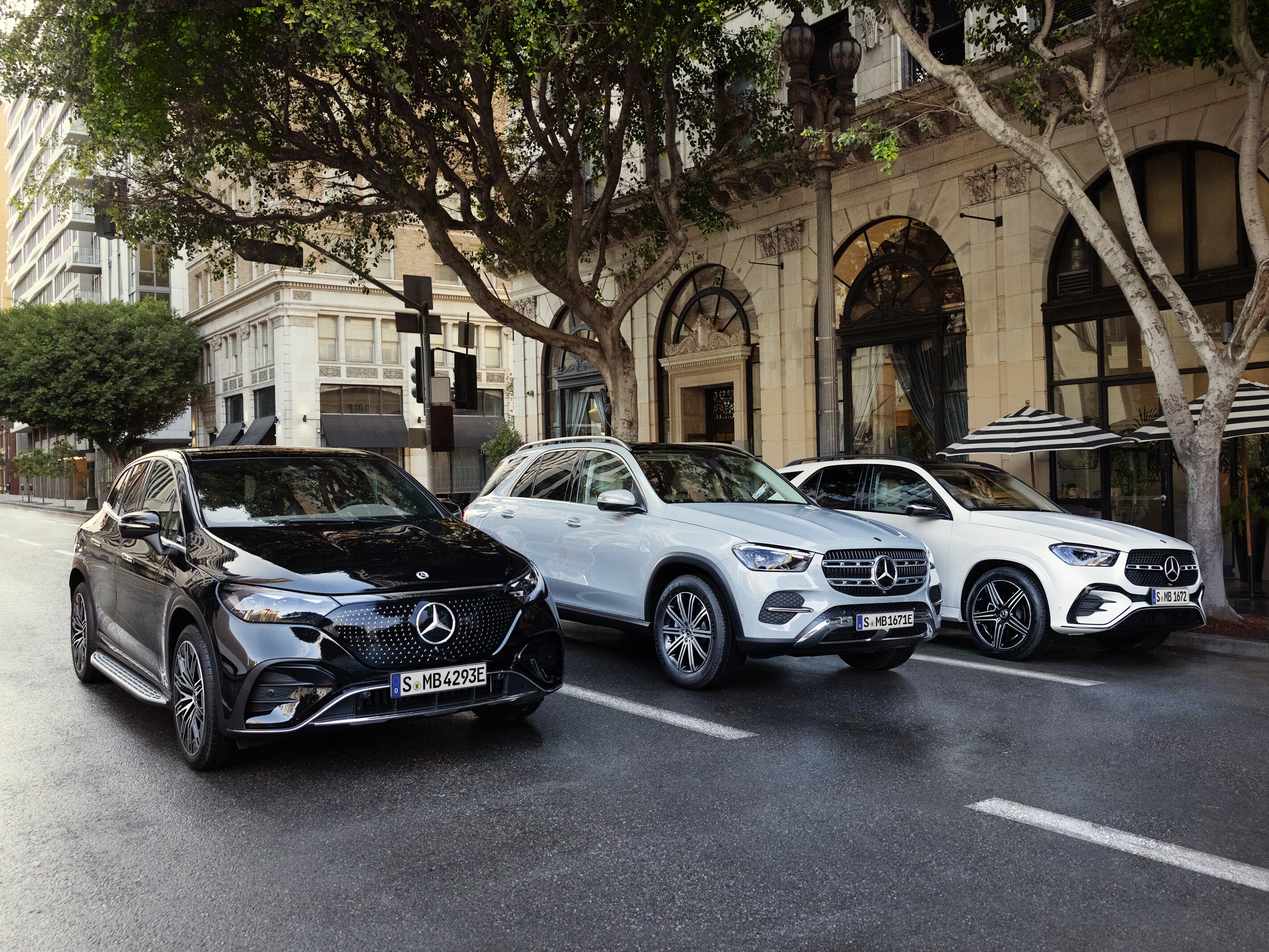 Tre olika Mercedes-Benz modeller sida vid sida på en väg i storstad.