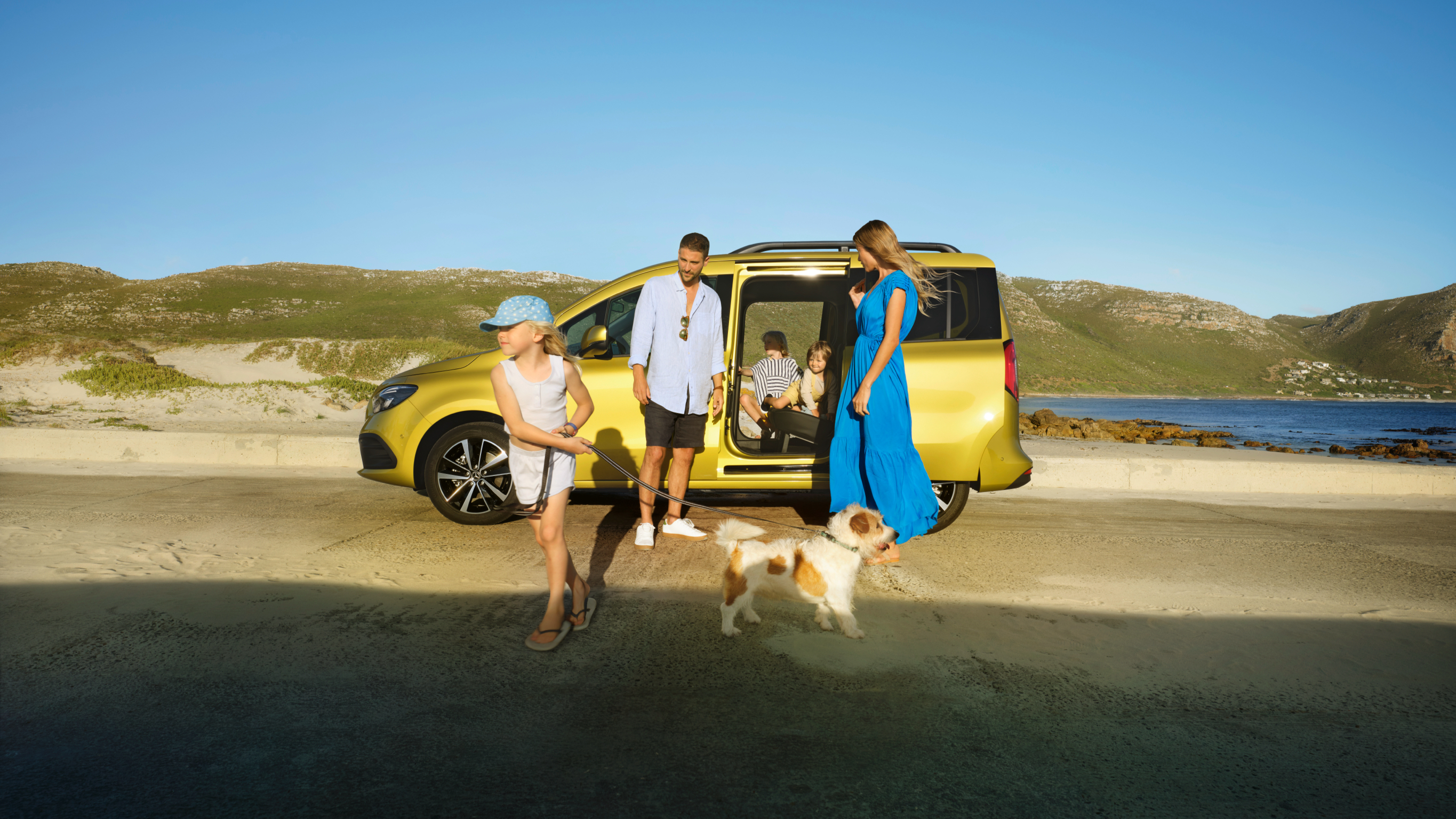 Familjebilar med 7 sittplatser | Mercedes-Benz En familj med hund på stranden framför sin gula Mercedes-Benz T-klass