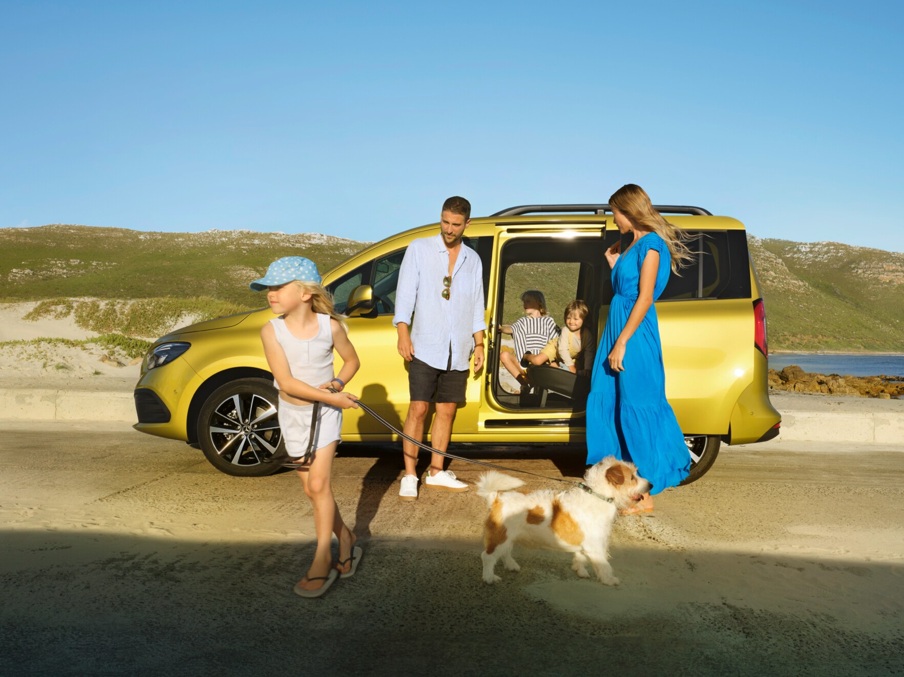En familj med hund på stranden framför sin gula Mercedes-Benz T-klass