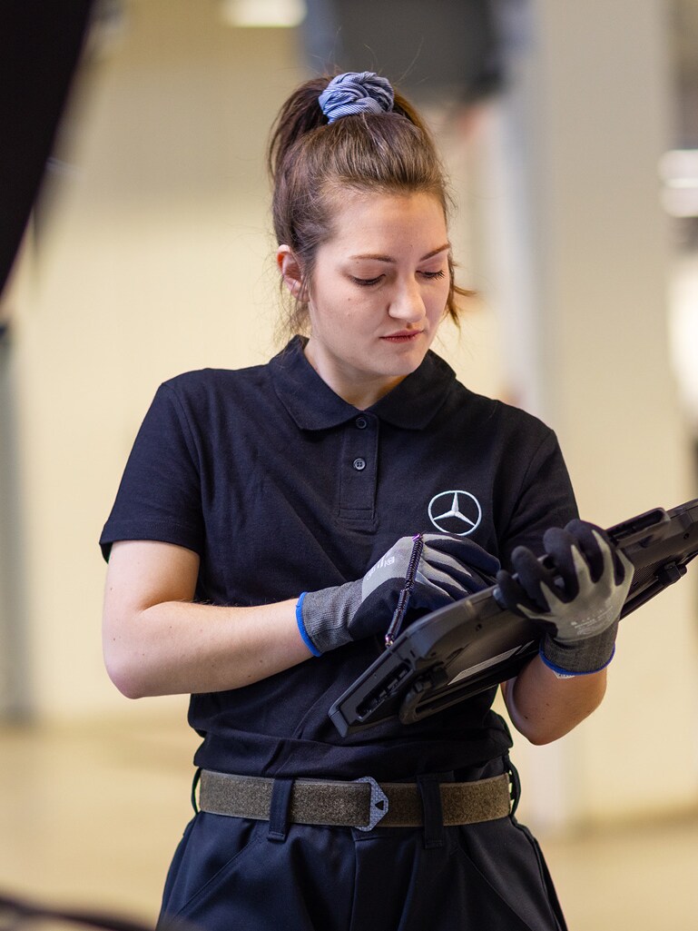 En kvinna i svart skjorta och handskar håller en laptop i sina händer.