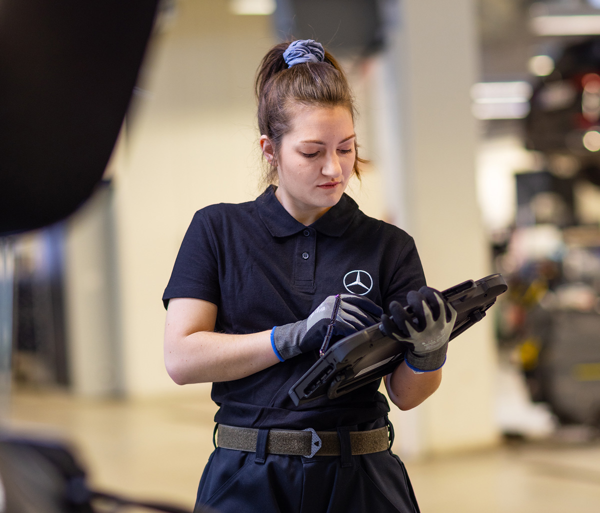 Serviceavtal till din Mercedes-Benz | Mercedes-Benz Finans En Mercedes-Benz mekaniker i svart skjorta håller en laptop i sina händer