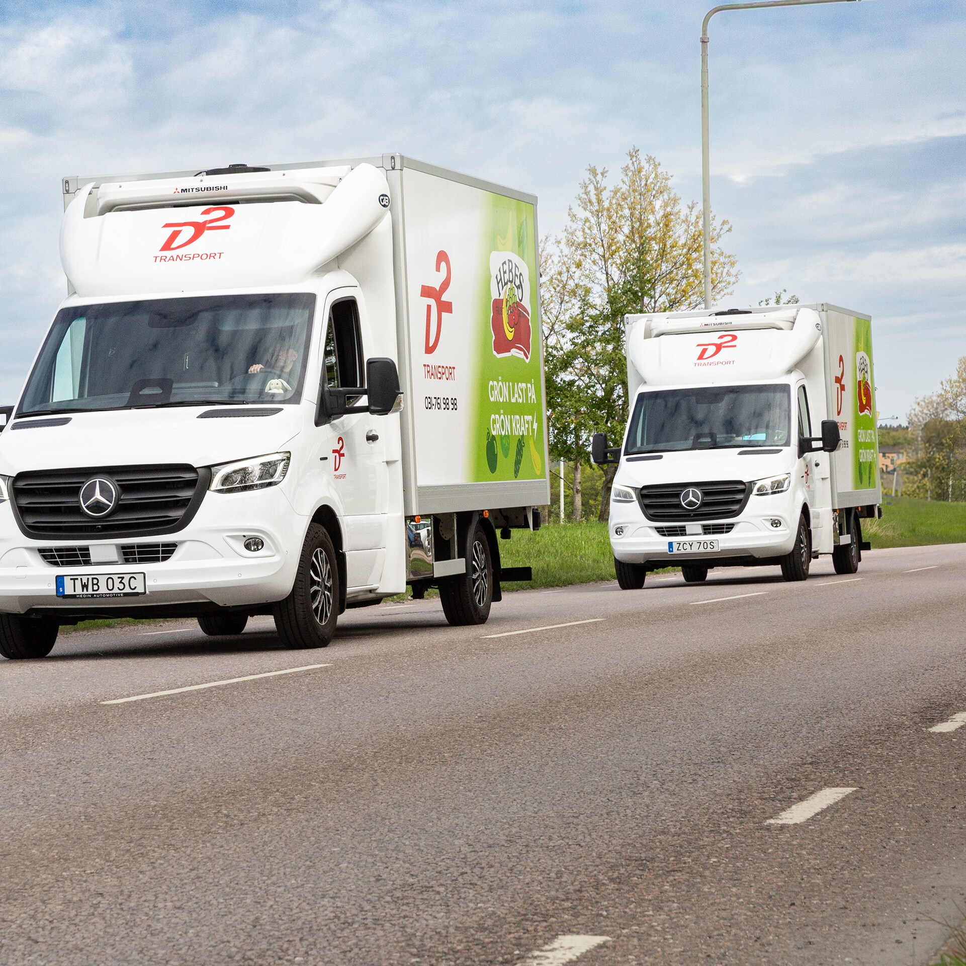 Två vita eldrivna transportbilar eSprinter från Mercedes-Benz kör på landsväg