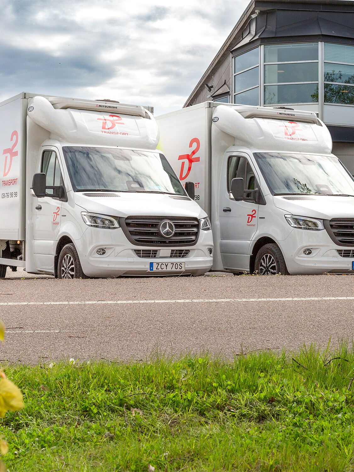 Två vita Mercedes-Benz eSprinter från D2 står parkerade utanför kontor