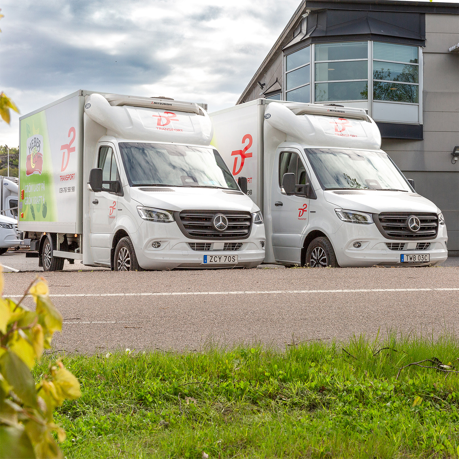 D2 Transport | Mercedes-Benz Transportbilar Två vita Mercedes-Benz eSprinter från D2 står parkerade utanför kontor
