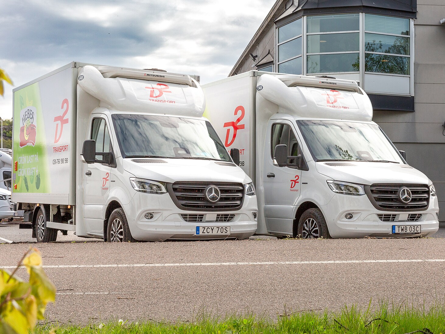 Två vita Mercedes-Benz eSprinter från D2 står parkerade utanför kontor