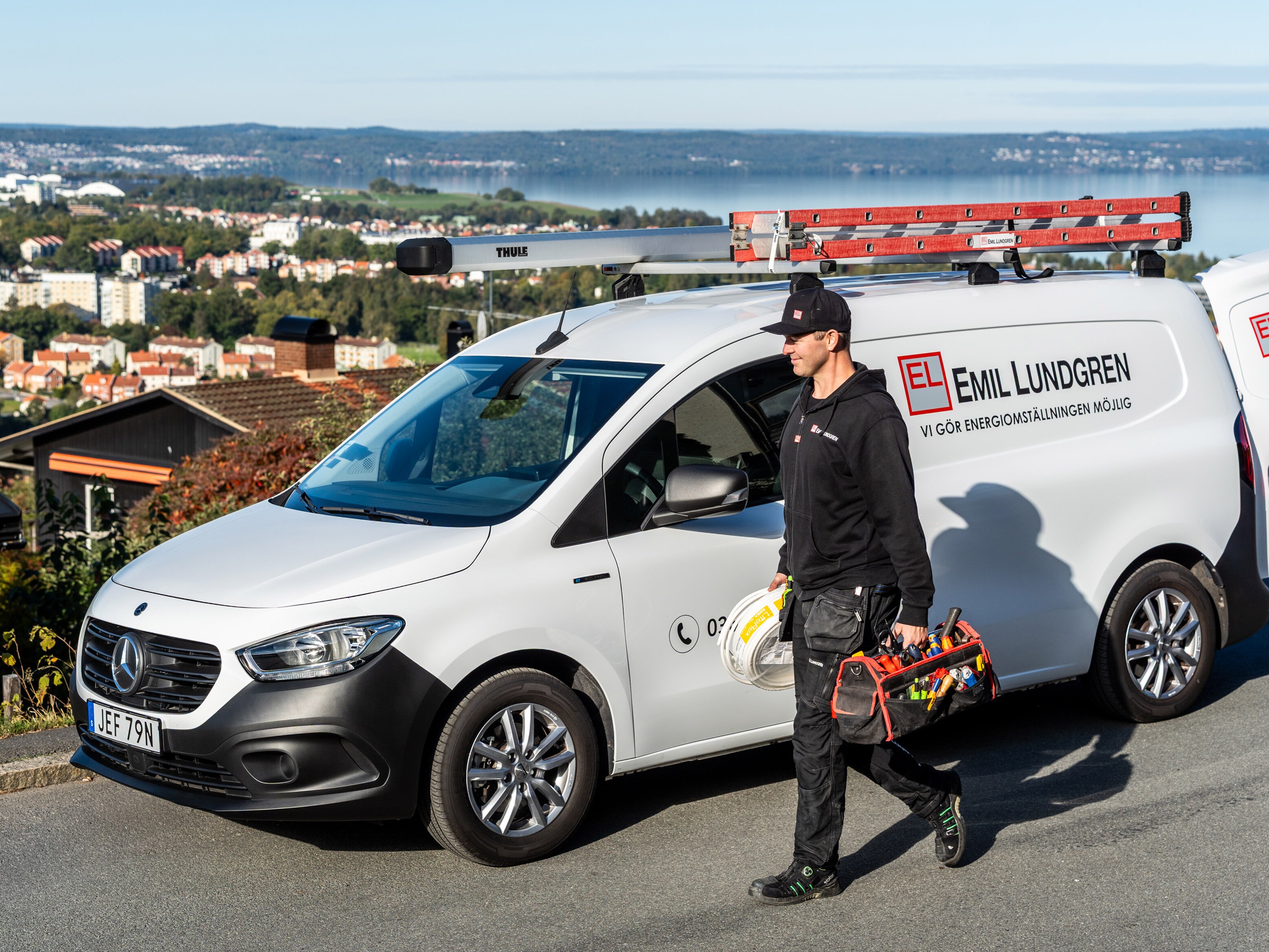 Eltekniker med utrustning i händerna står framför sin Mercedes-Benz transportbil.