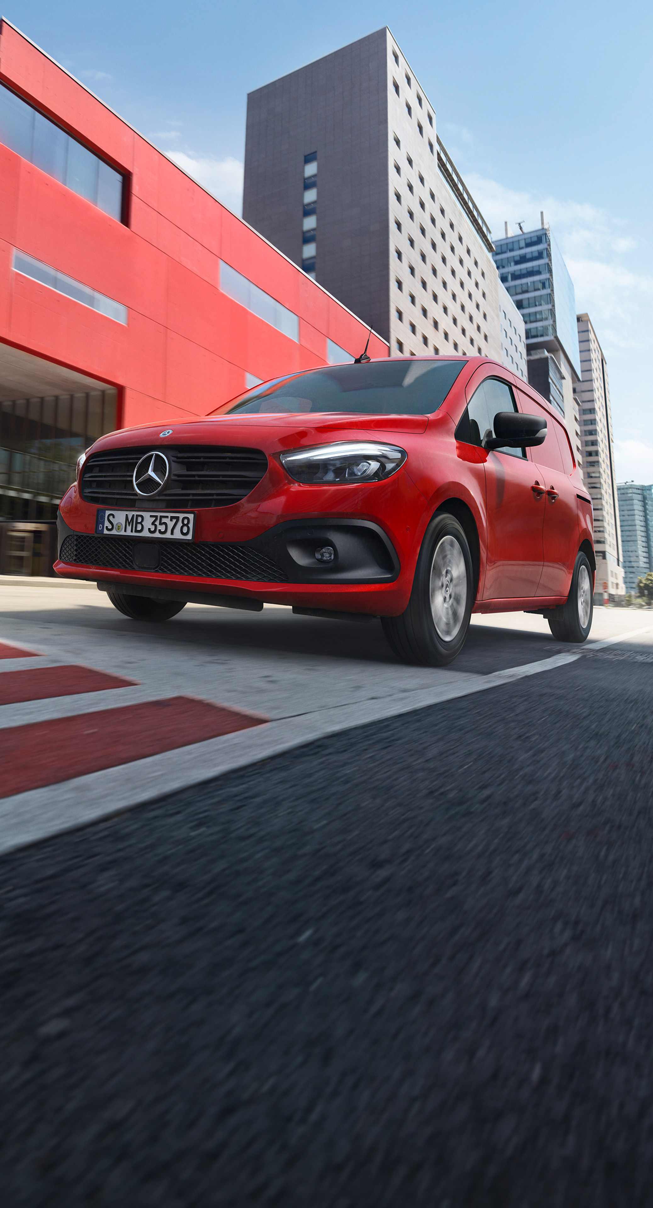 Röd Mercedes-Benz eCitan på väg framför röd byggnad