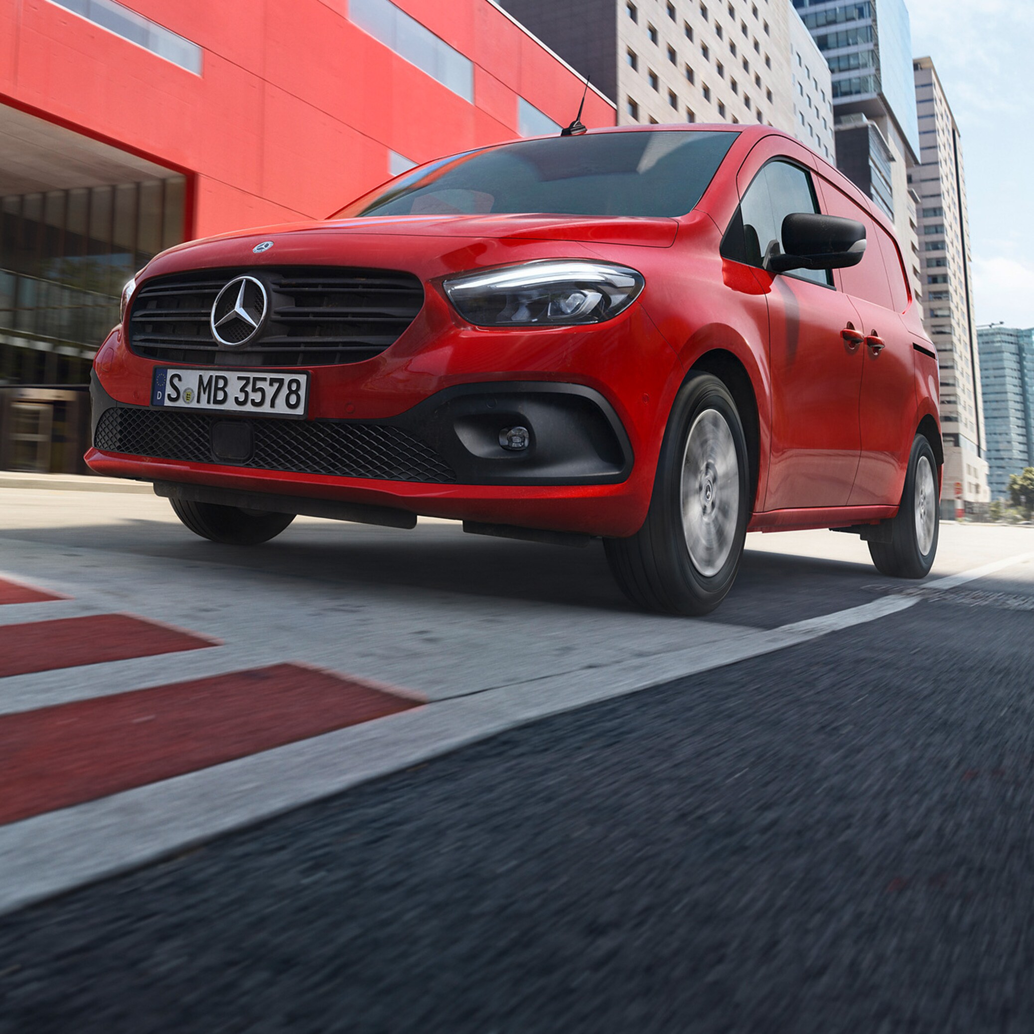 Röd Mercedes-Benz eCitan på väg framför röd byggnad