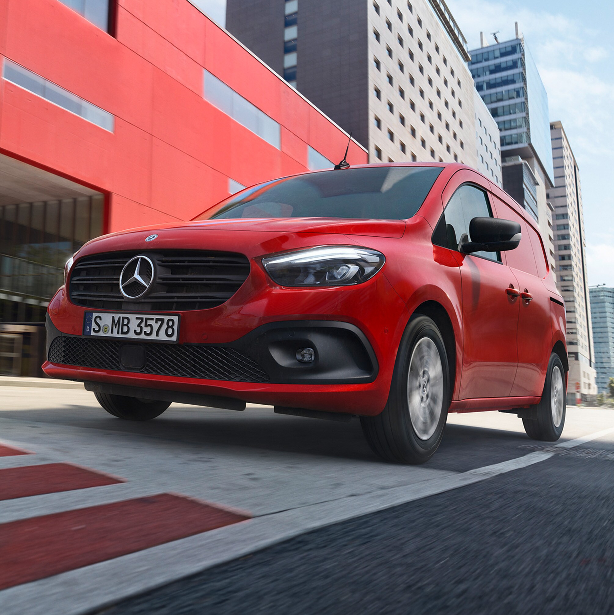 Röd Mercedes-Benz eCitan på väg framför röd byggnad