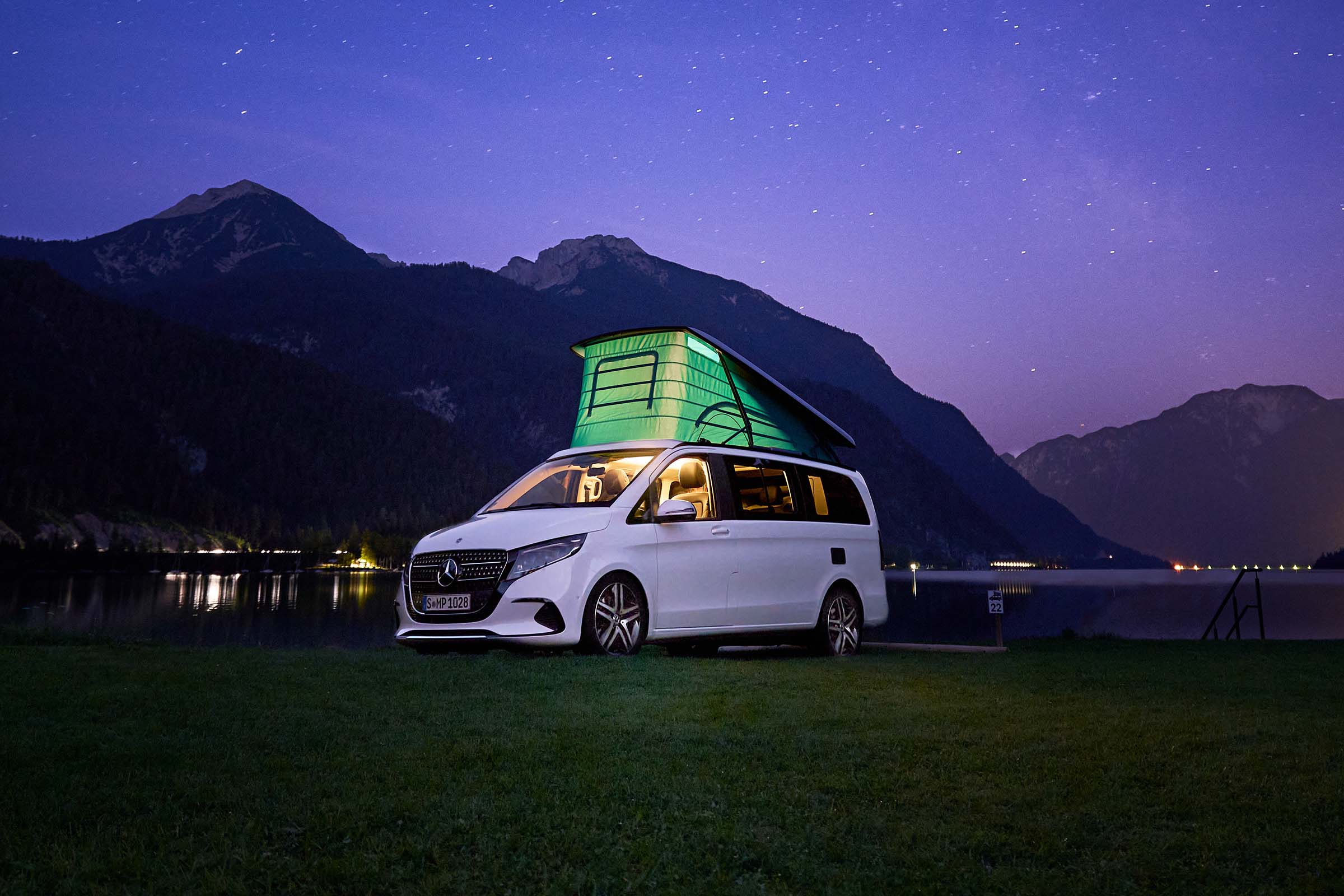 Elmia Husvagn Husbil | Marco Polo | Mercedes-Benz Transportbilar Vit Marco Polo-campingbuss vid en sjö med uppfällt tak.
