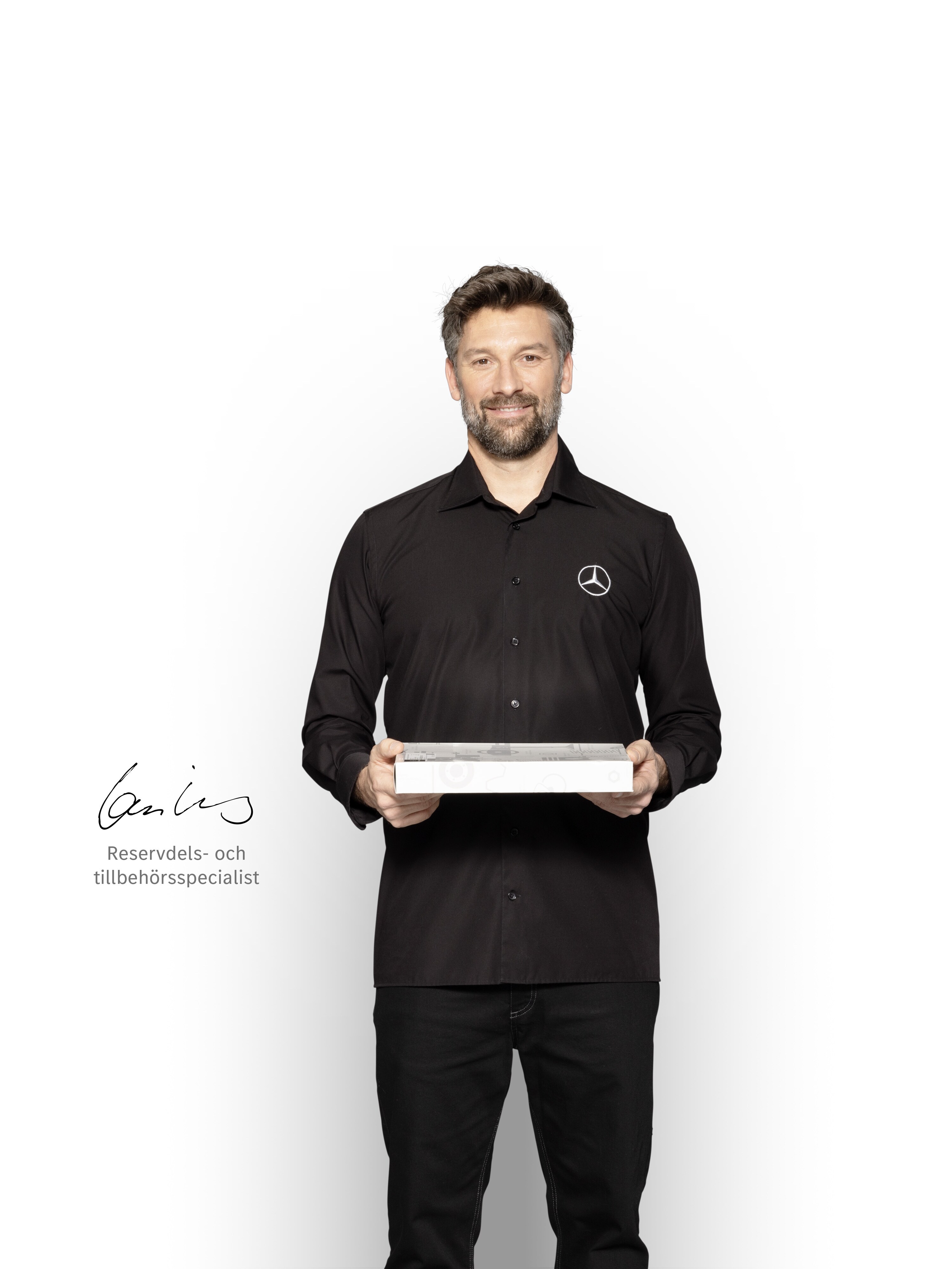 Intern tekniker på Mercedes-Benz med en låda i handen för att visa Mercedes-Benz originaldelar.